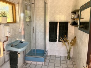 Ein Badezimmer mit einer Duschkabine aus Glas, einem Waschbecken mit blauer Schale und einem gefliesten Boden.
