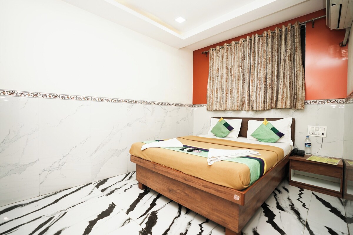 A hotel room with a bed, a nightstand, a wall-mounted air conditioner, and a curtain.