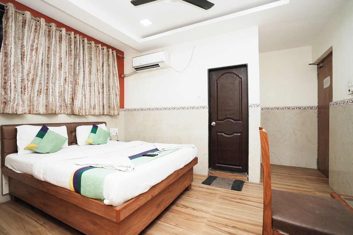 A neatly made bed with a wooden frame, a dark door, and a chair in a room with a tiled floor and a ceiling fan.