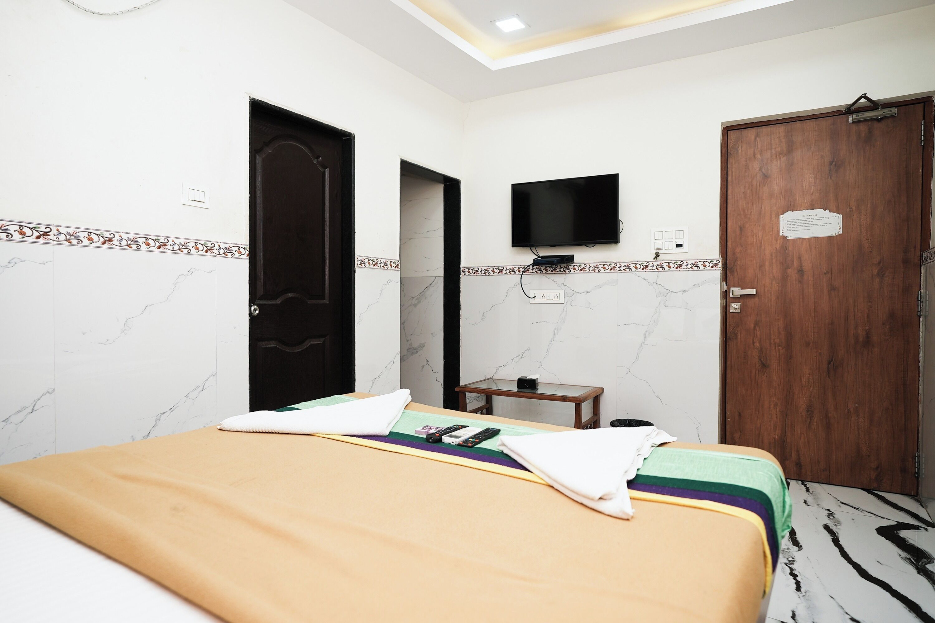 A hotel room with a bed, a television mounted on the wall, a wooden door, and a small table.