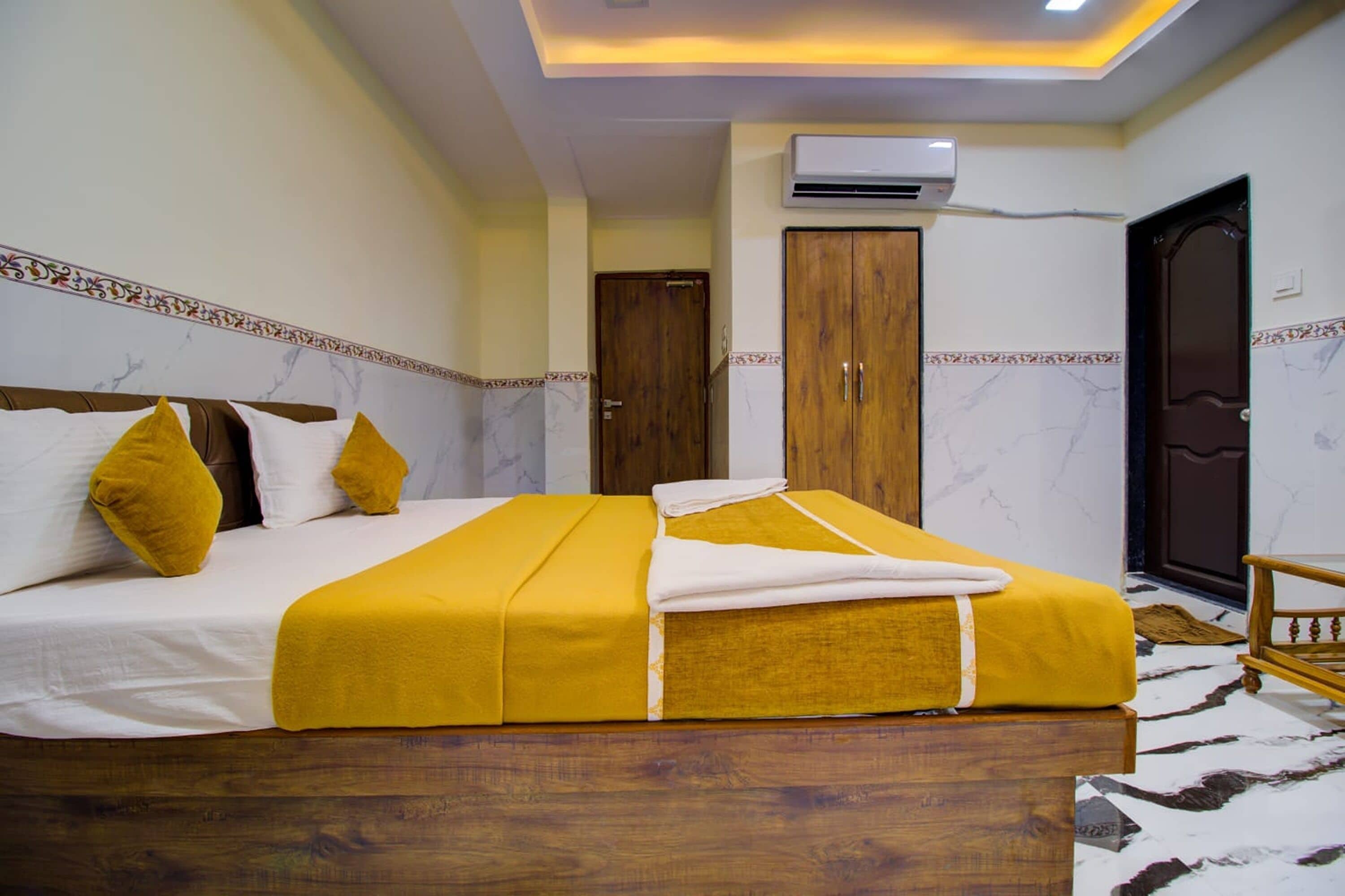 A hotel room with a large bed, a wooden wardrobe, an air conditioning unit, and a door.
