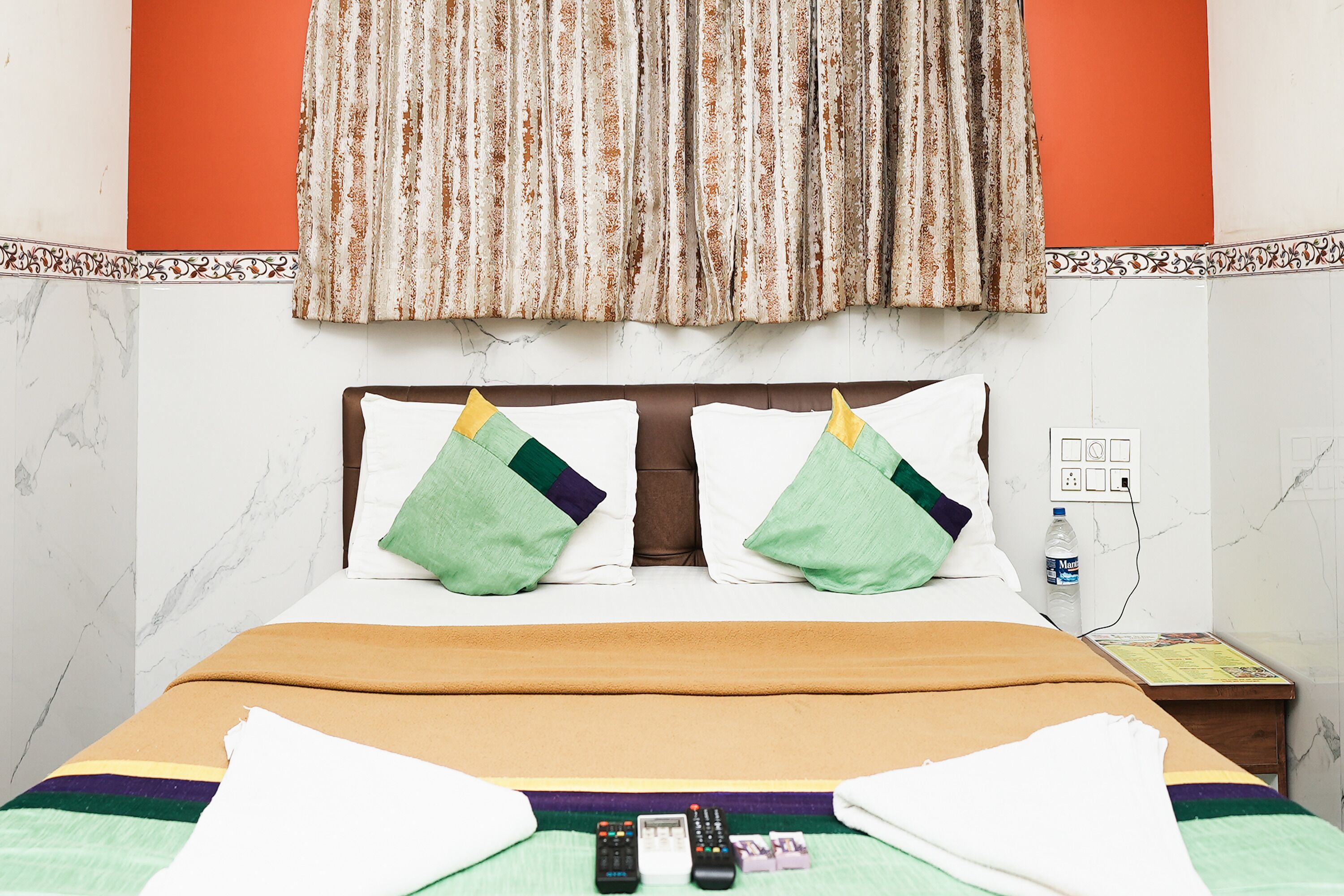 A hotel room with a bed, pillows, a blanket, a water bottle, and a nightstand.