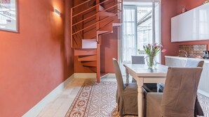 Cocina compacta con escalera espiral, zona de comedor con mesa y sillas, y vista a través de un ventanal.
