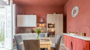 Una cocina compacta con comedor, microondas, un reloj y un florero con flores.