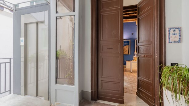 Entrada de hotel con puerta de vidrio, puerta de madera marrón y pared azul con un cuadro enmarcado.