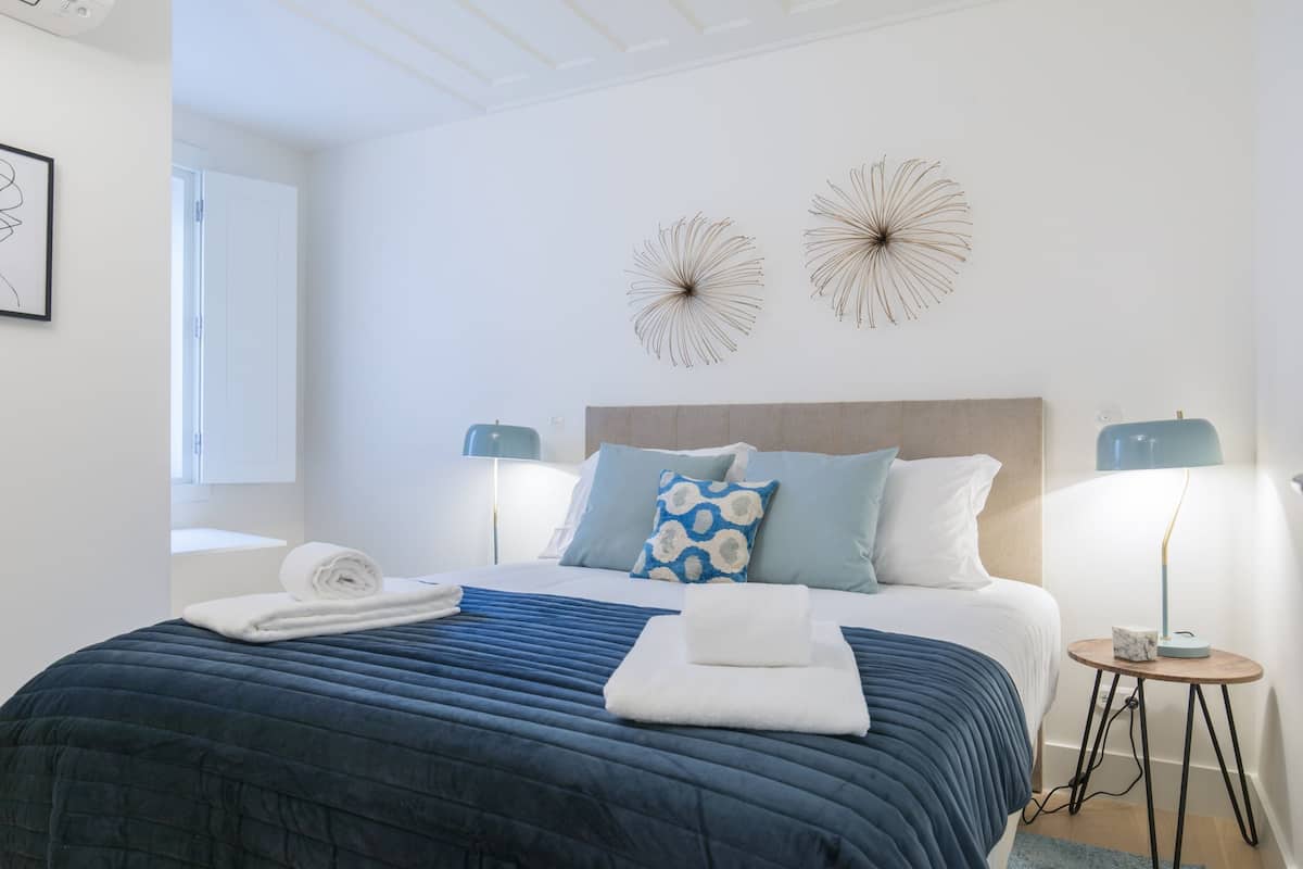A neatly made bed with a blue and white duvet, two wall art pieces, and two bedside lamps.