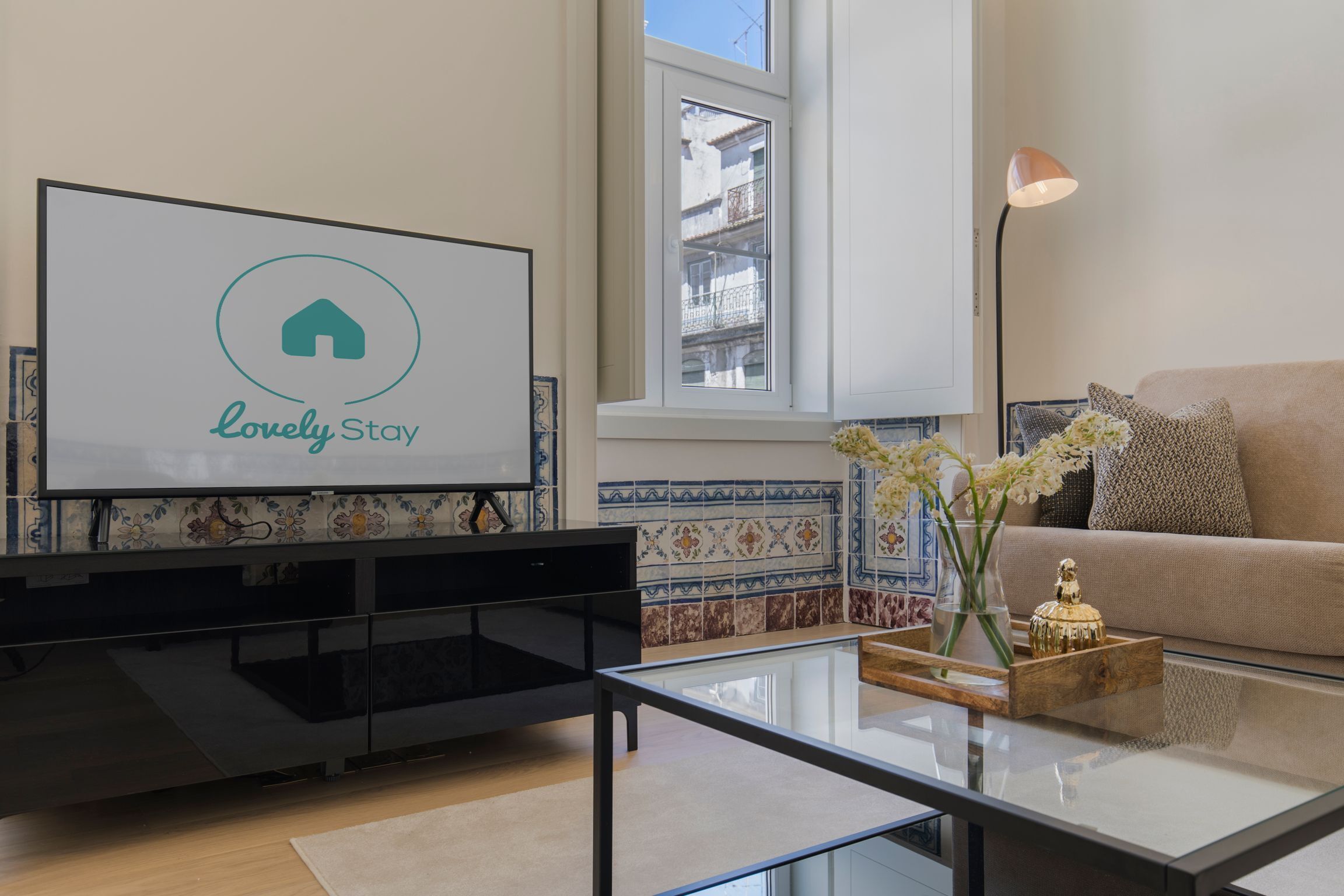 Una sala de estar moderna con un televisor de pantalla plana, una mesa de centro de vidrio, un sofá color beige y un jarrón decorativo.