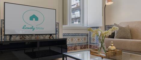 Una sala de estar moderna con un televisor de pantalla plana, una mesa de centro de vidrio, un sofá color beige y un jarrón decorativo.