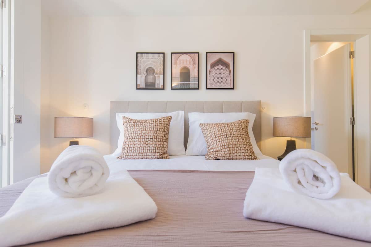 A hotel room with a bed, two pillows, two lamps, and three framed pictures on the wall.