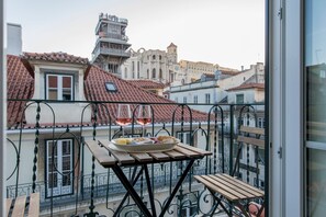 A balcony with a table set for two, overlooking a cityscape with historic buildings. - Ando Living Santa Justa 79 House (Lisbon)