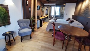 A modern hotel room with a wooden ceiling, a bed with a grey bedspread, a dining area with a wooden table and chairs, and a small kitchen area. - La Jacquière - Chambres de charme (Chaumont-sur-Loire)