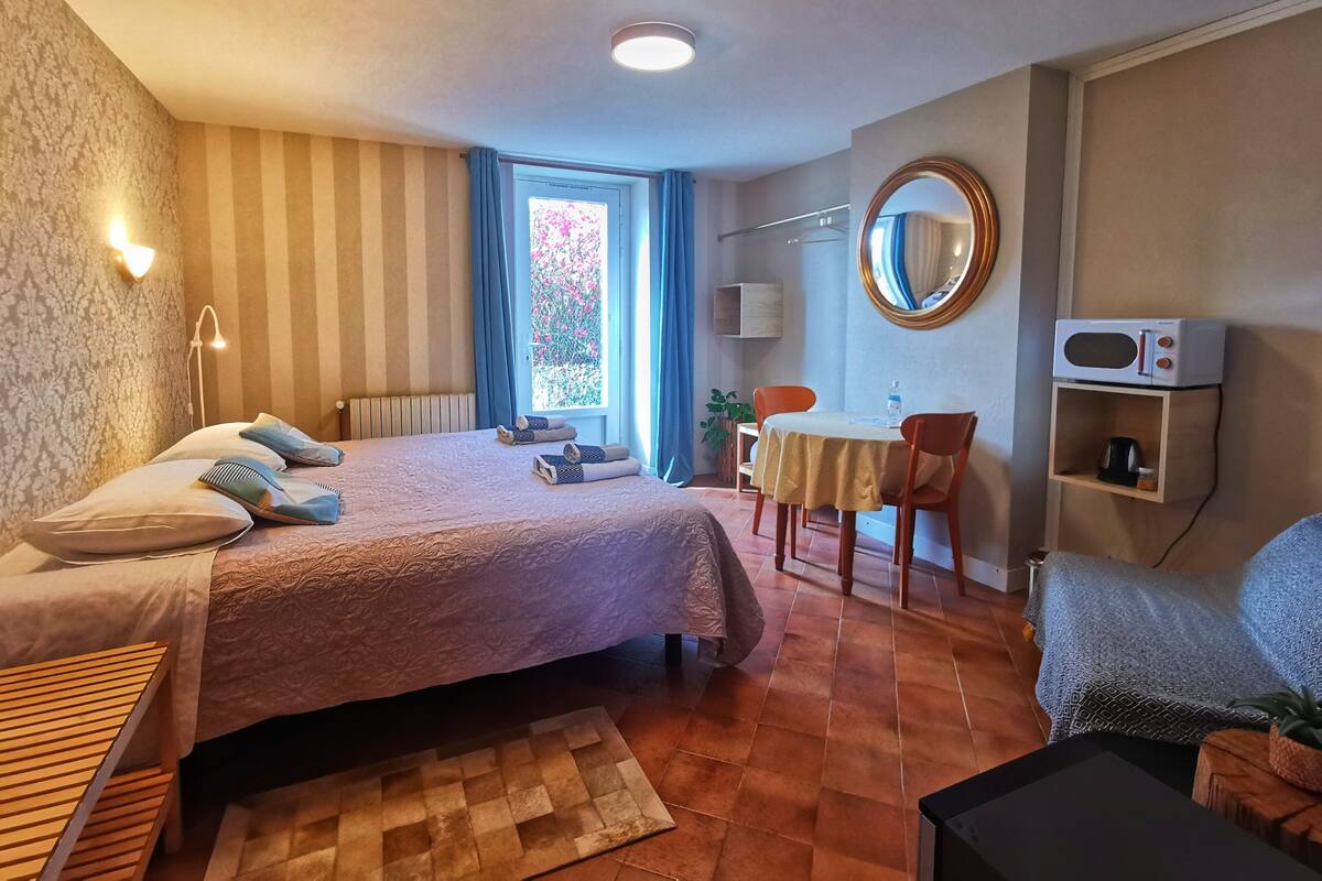 Habitación de hotel con cama, escritorio, silla, espejo redondo, microondas y ventana con cortinas.