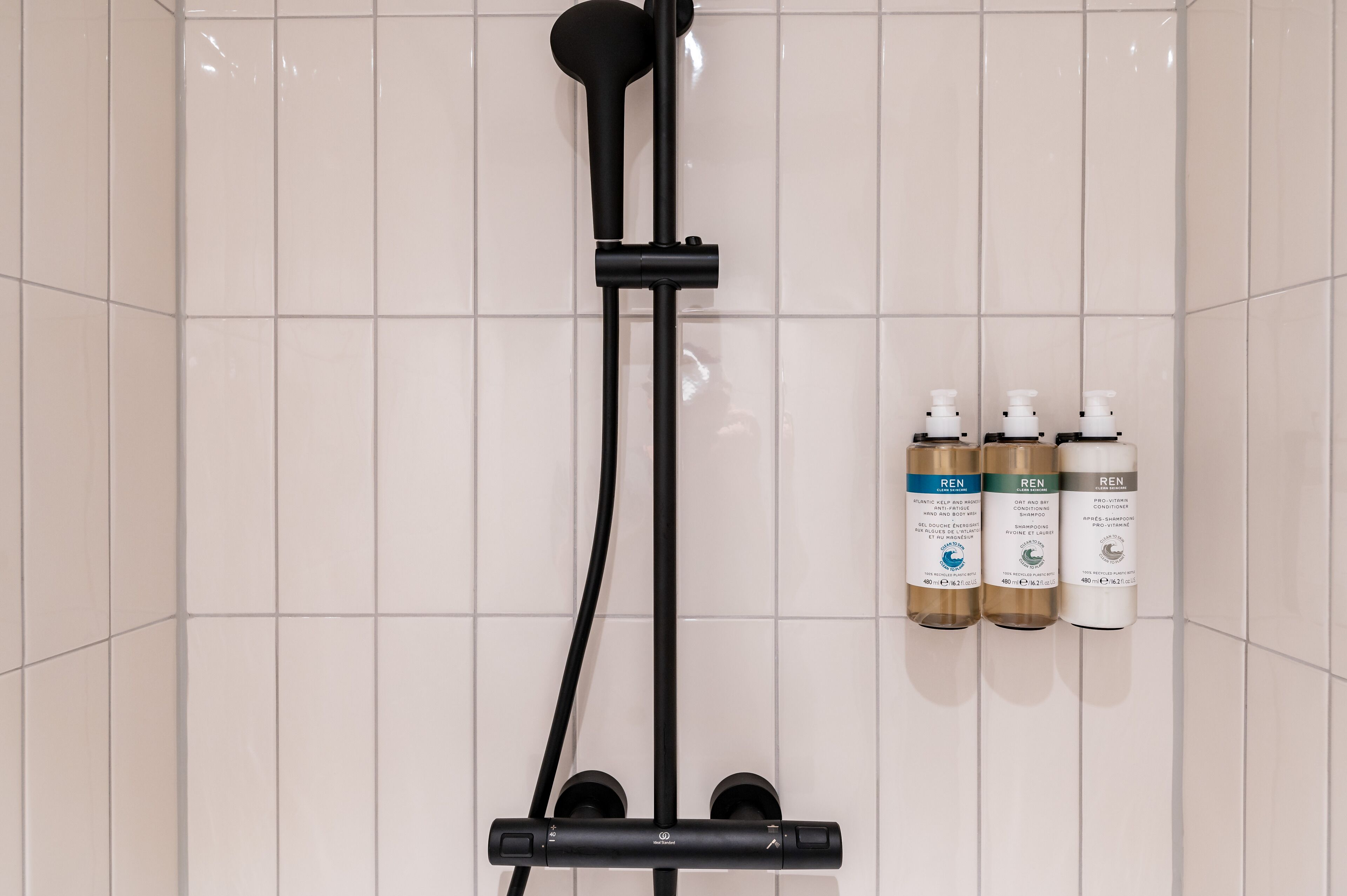 A shower area with a black hose and three bottles of REN products on the wall.