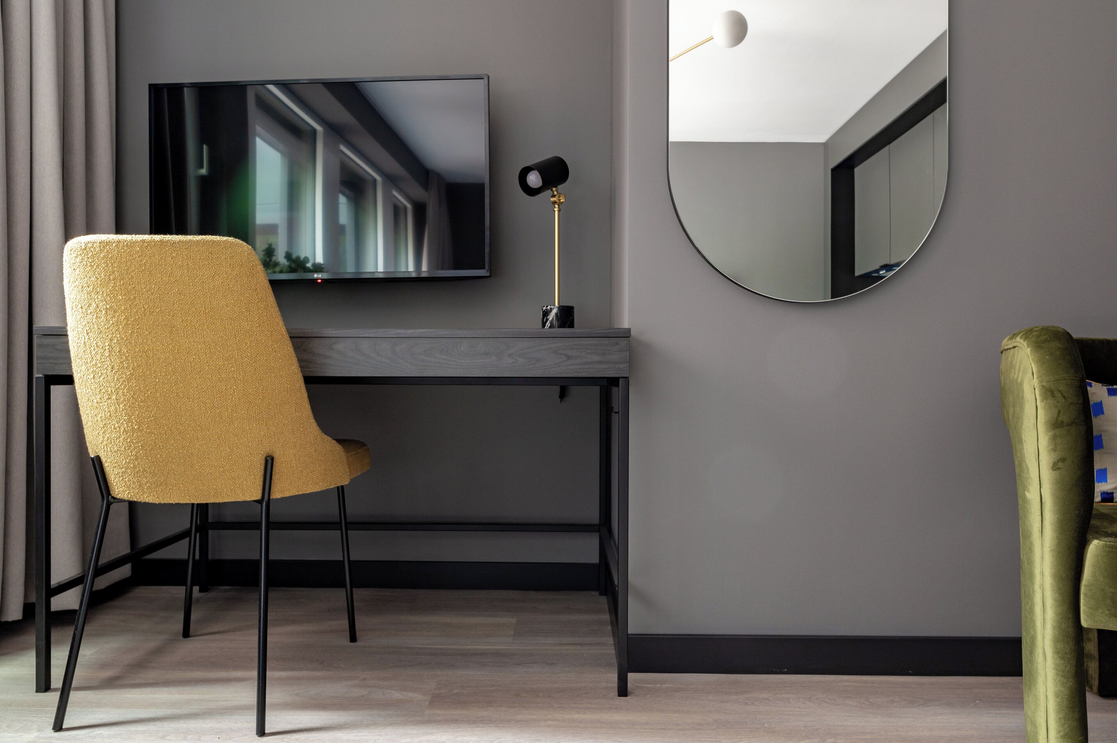 A modern room with a desk, a television, a round mirror, and two chairs.
