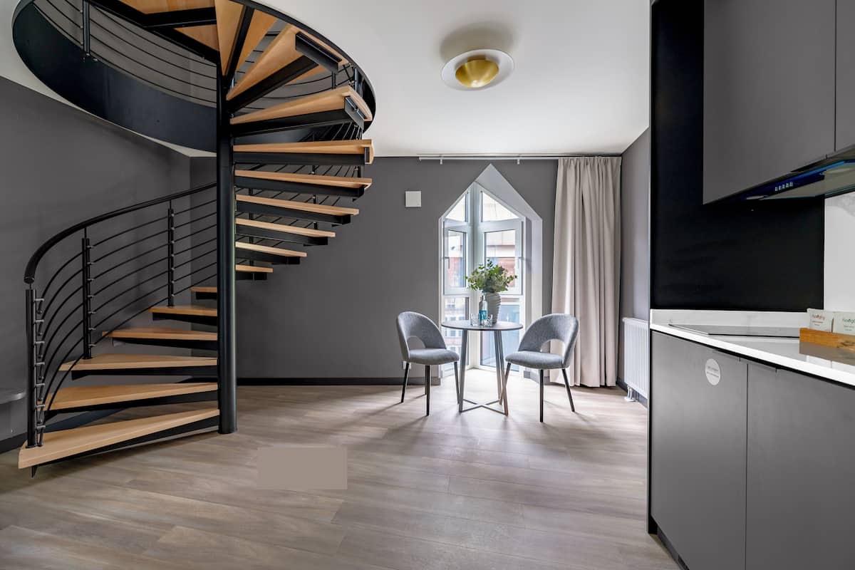 A modern kitchen with a spiral staircase, a dining area with two chairs, and a large window.