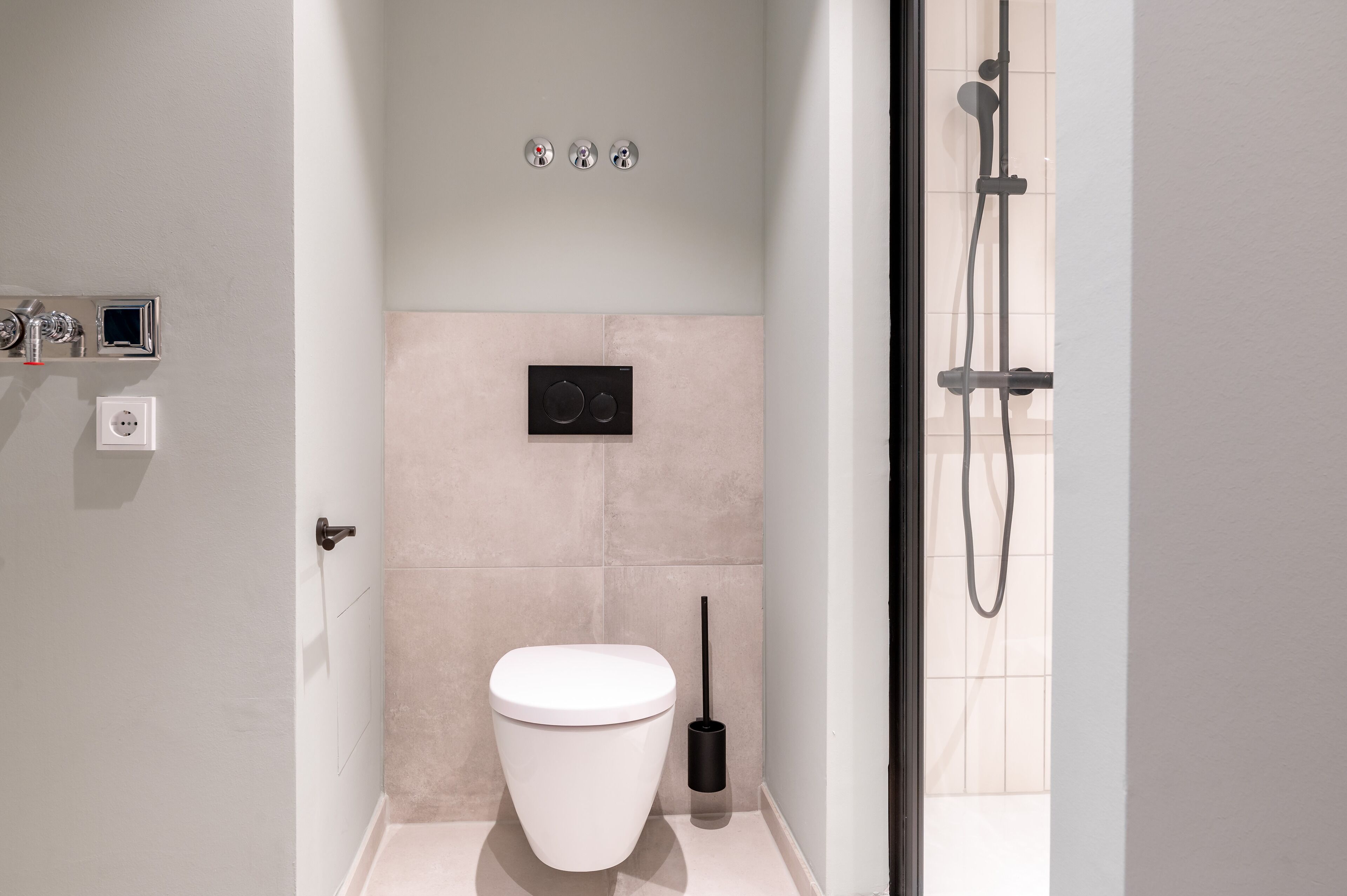 A modern bathroom with a white toilet, a black bidet, and a handheld showerhead.