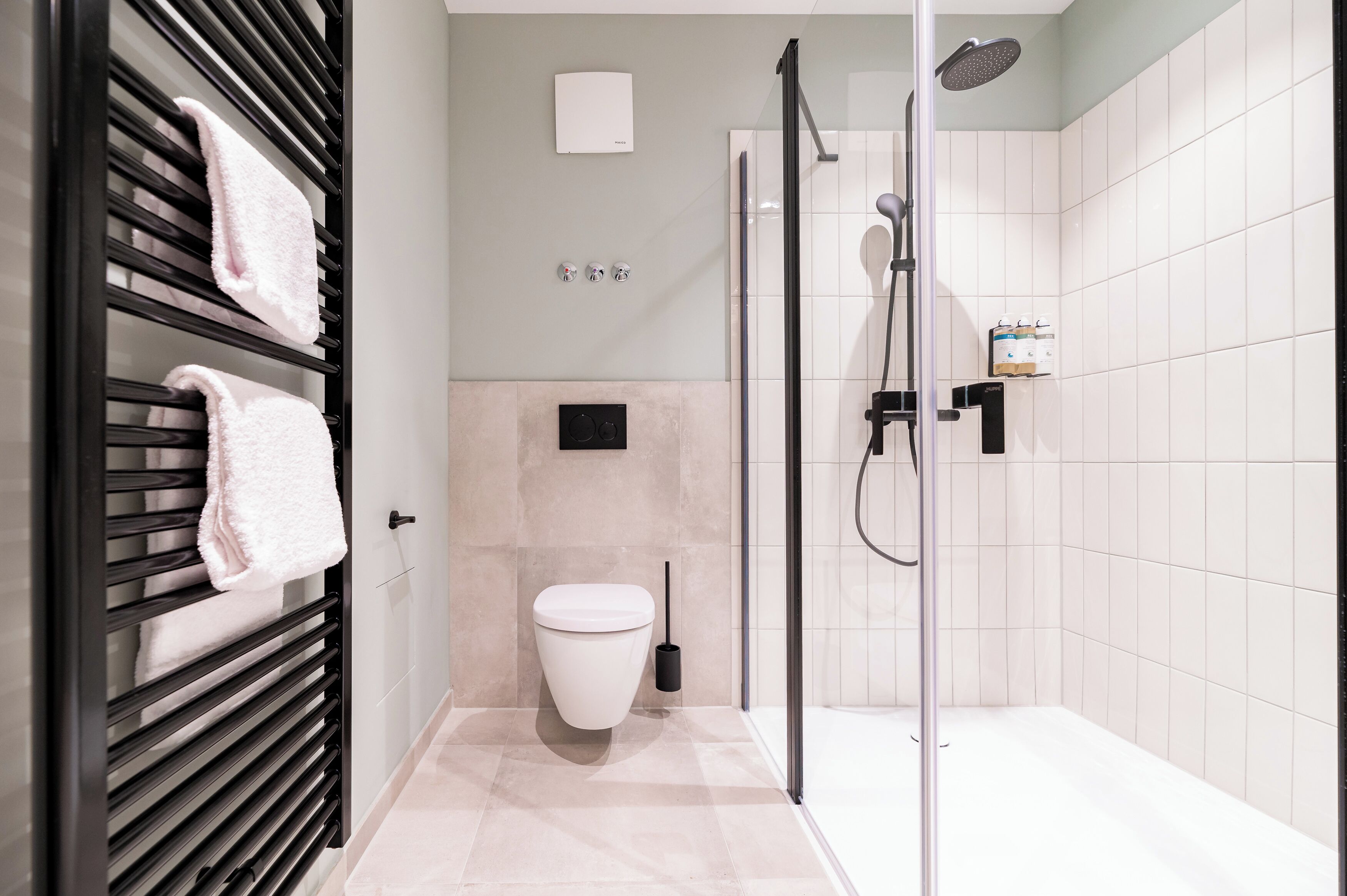 A modern bathroom with a glass-enclosed shower, a toilet, and a towel rack with towels.