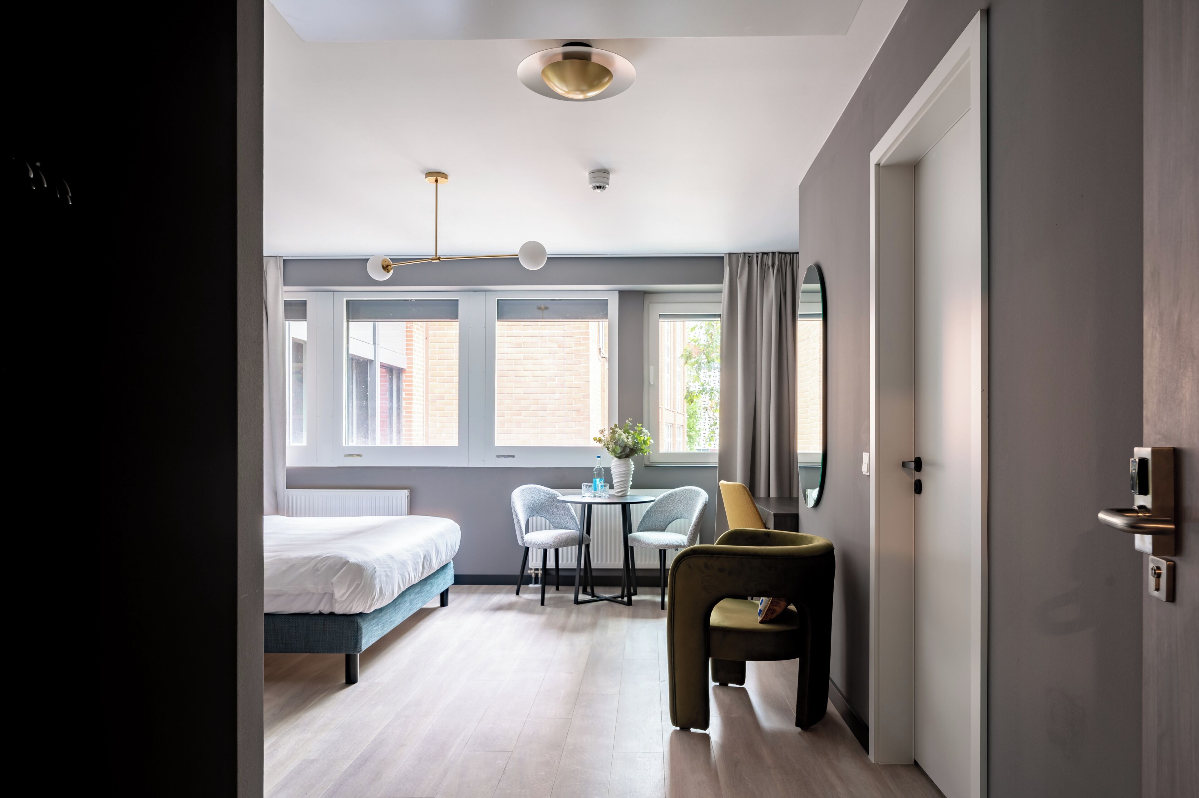 Una habitación de hotel moderna con cama, una pequeña mesa con sillas, un espejo y una puerta con cerradura.