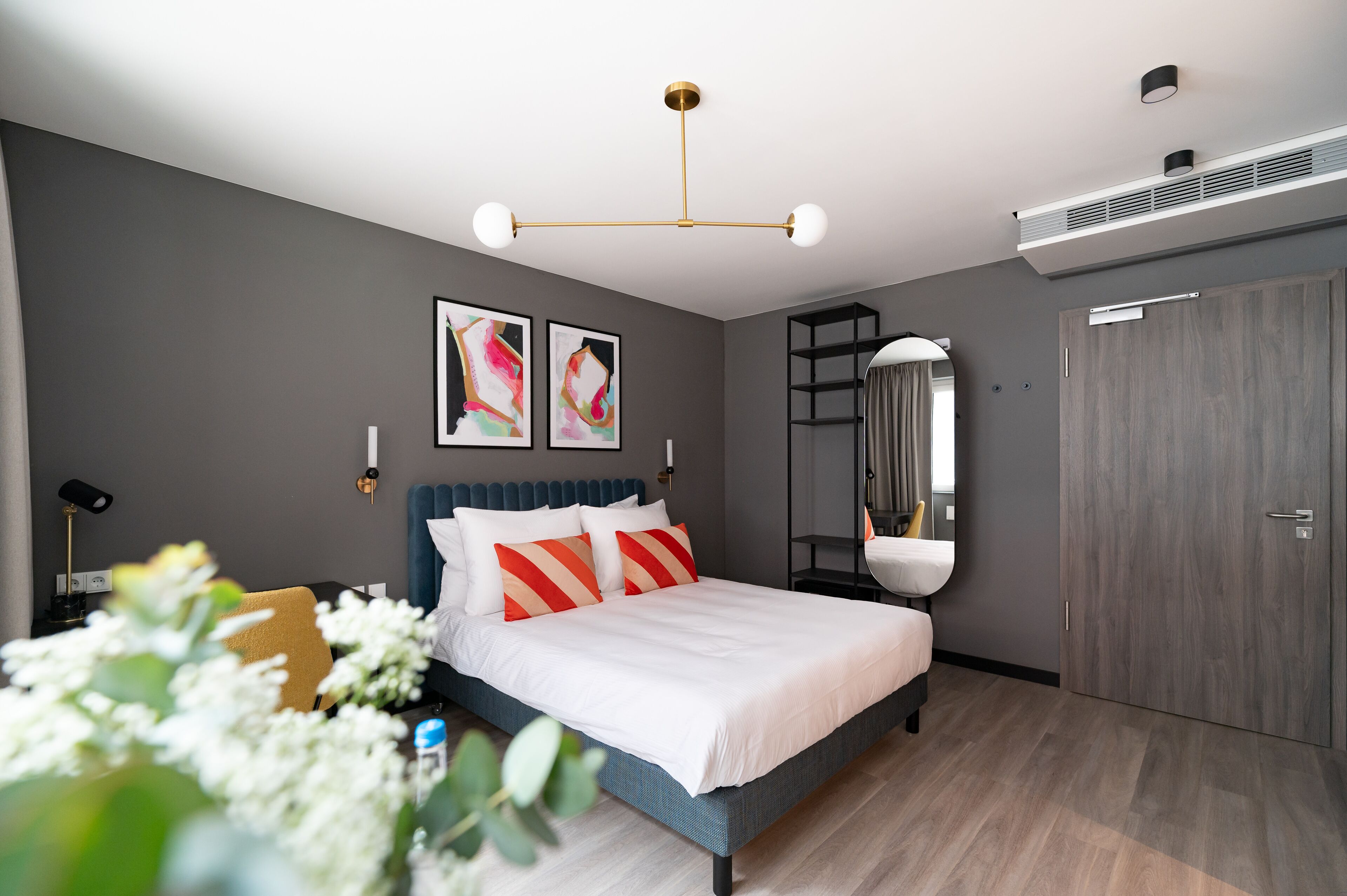 A modern bedroom with a bed, a bedside table, a mirror, and a wardrobe.