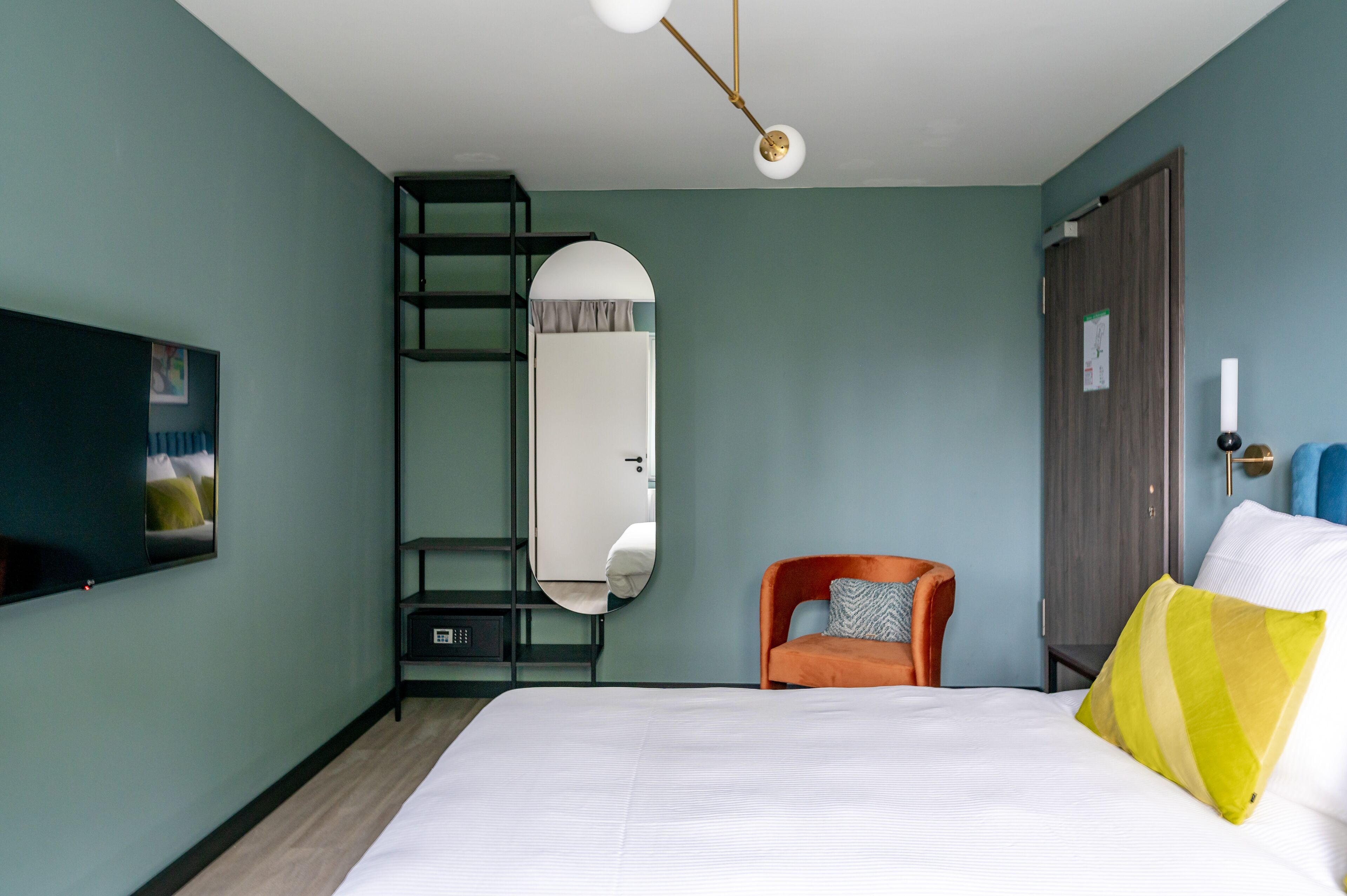 A bedroom with a bed, a chair, a mirror, a wardrobe, and a television on the wall.