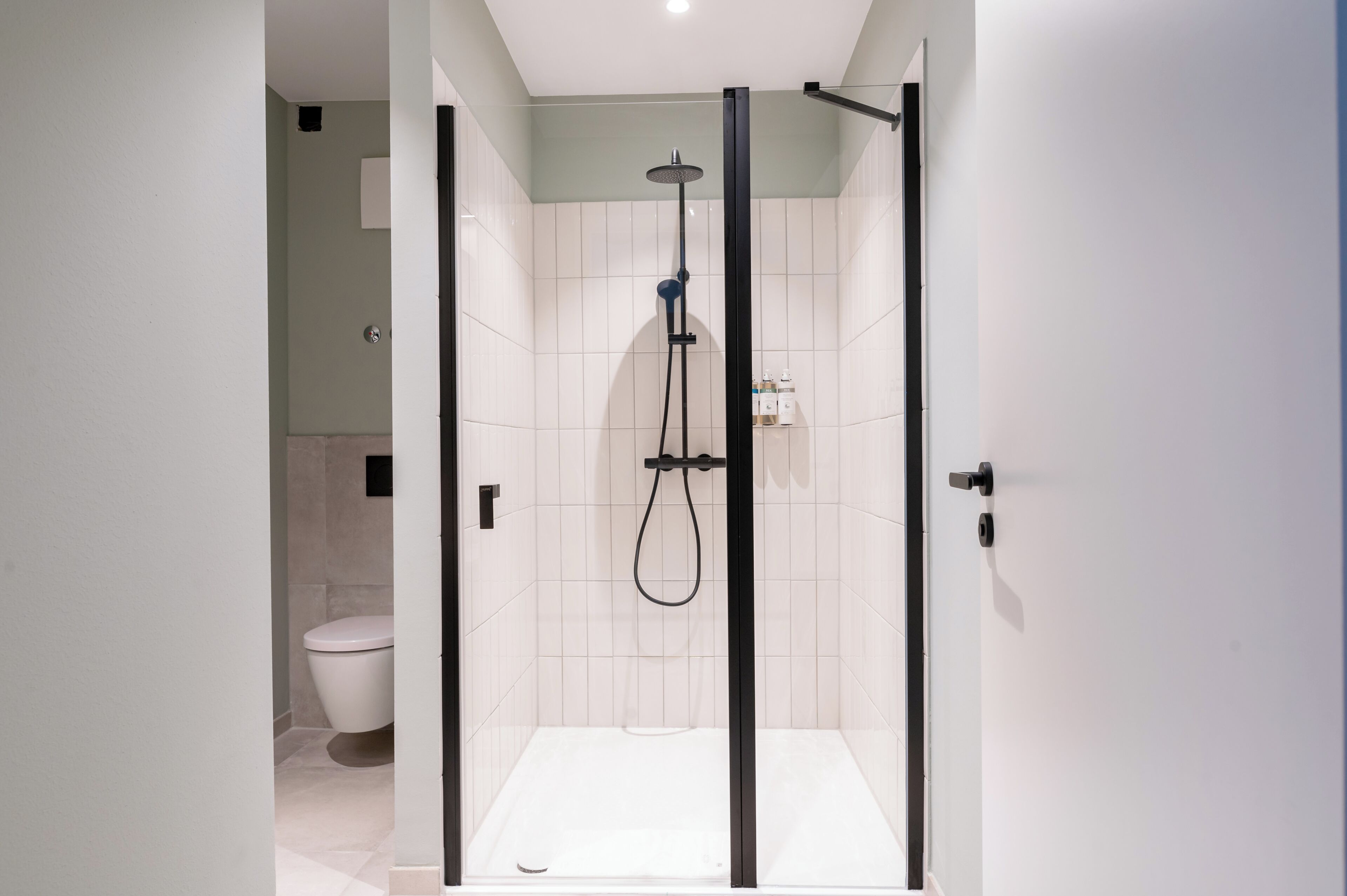 A modern bathroom with a glass-enclosed shower, a toilet, and a white tiled wall.