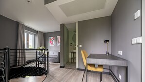 A modern living room with a staircase, a dining area with a table and chair, and a view of the outside through a window.