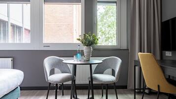 Una habitación moderna con una mesa redonda, dos sillas, un florero con flores, una botella de agua y un televisor.