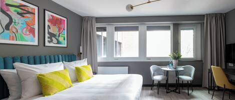 Un dormitorio moderno con una cama grande, un escritorio con dos sillas, un ventanal con cortinas y arte abstracto en la pared.