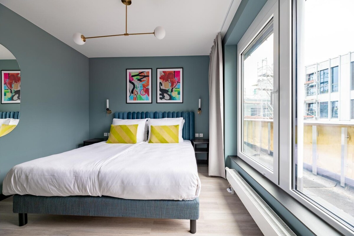 A modern bedroom with a large bed, two bedside tables, and a view of the city through a large window.