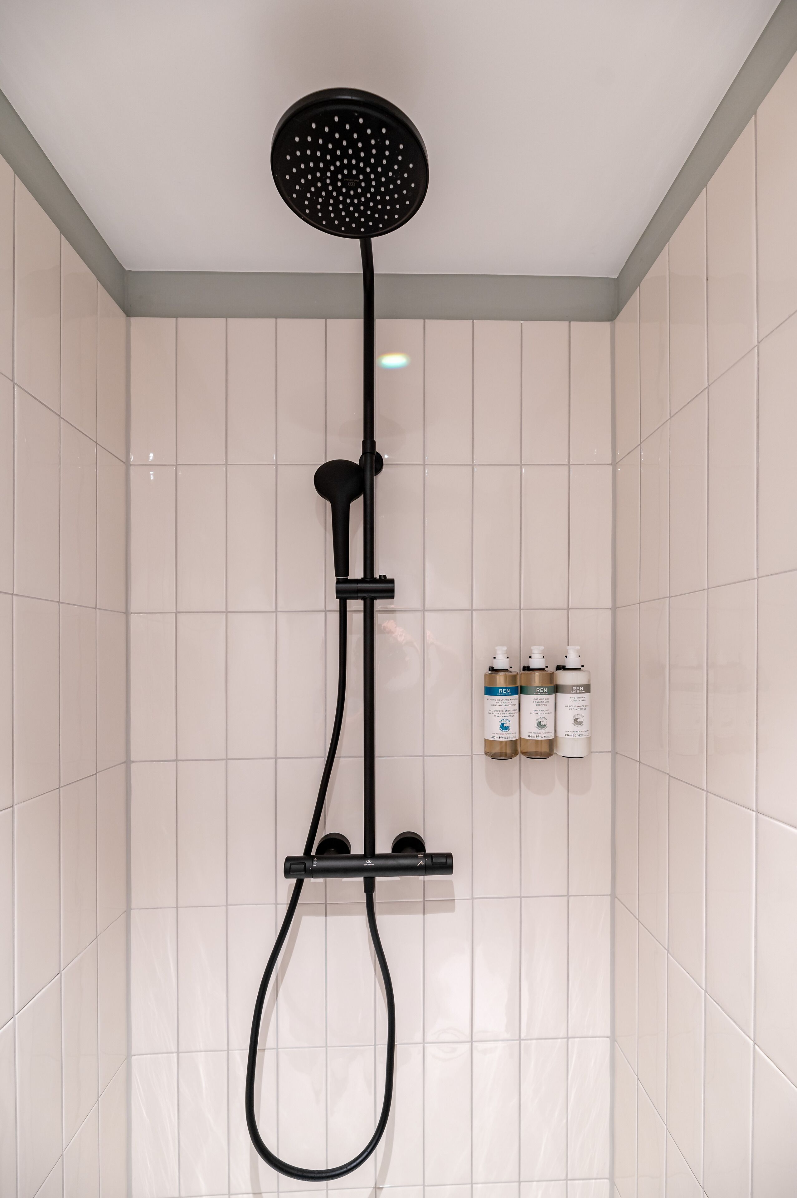 A modern shower with a roundhead showerhead and a handheld shower attachment. There are three bottles of toiletries on a shelf to the right.