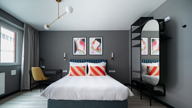 A modern bedroom with a bed, a desk, and a chair. There are two abstract paintings on the wall.