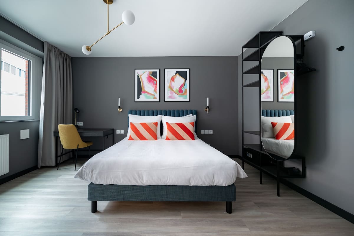 A modern bedroom with a bed, a desk, and a chair. There are two abstract paintings on the wall.