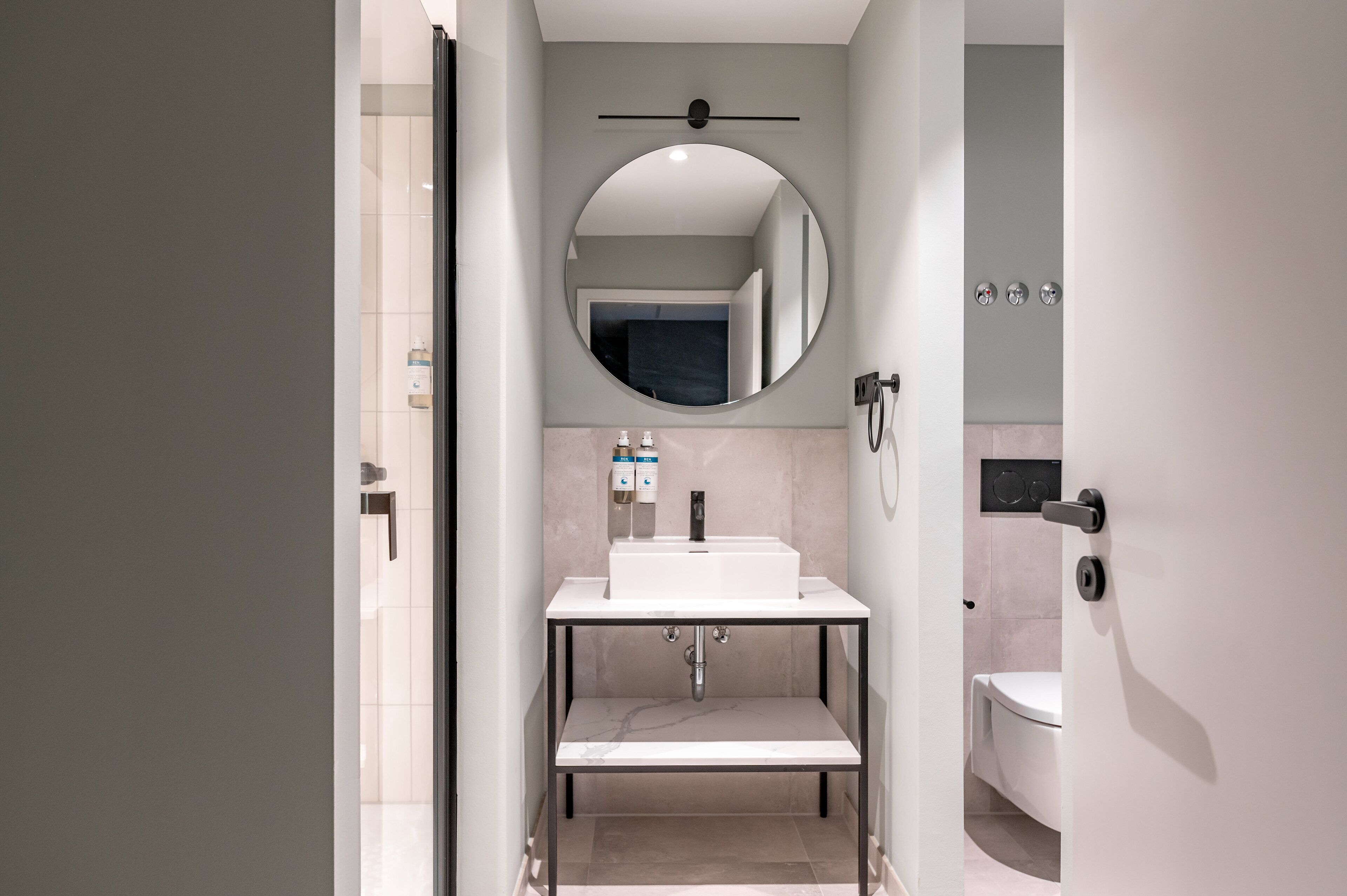 Ein modernes Badezimmer mit einem weißen Waschbecken, einem runden Spiegel und einer Toilette.