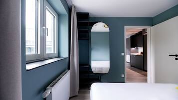 A bedroom with a large window, a mirror, and a door leading to a kitchen.