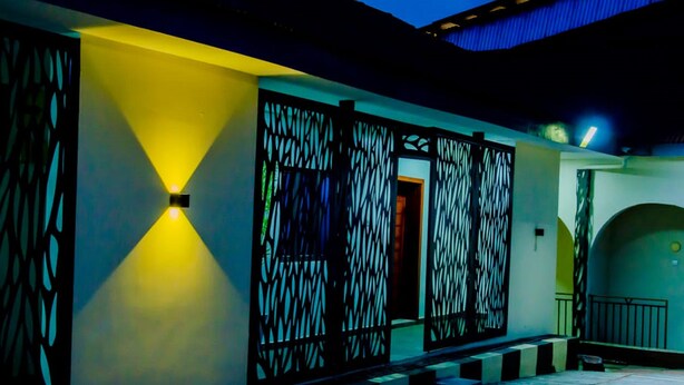 A building facade with a geometric metal gate and a yellow-lit wall. - Horizon Suites (Ibadan)