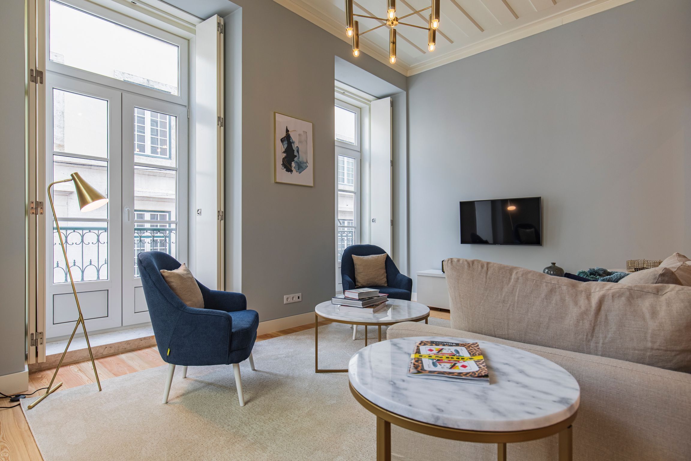 A modern living room with a sofa, two armchairs, a coffee table, and a TV mounted on the wall.