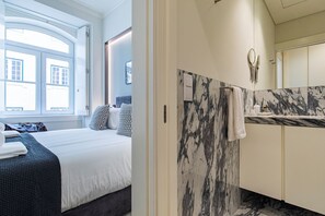 A hotel room with a bed, a window, a bathroom with a marble countertop and a mirror. - Ando Living São Nicolau House (Lisbon)