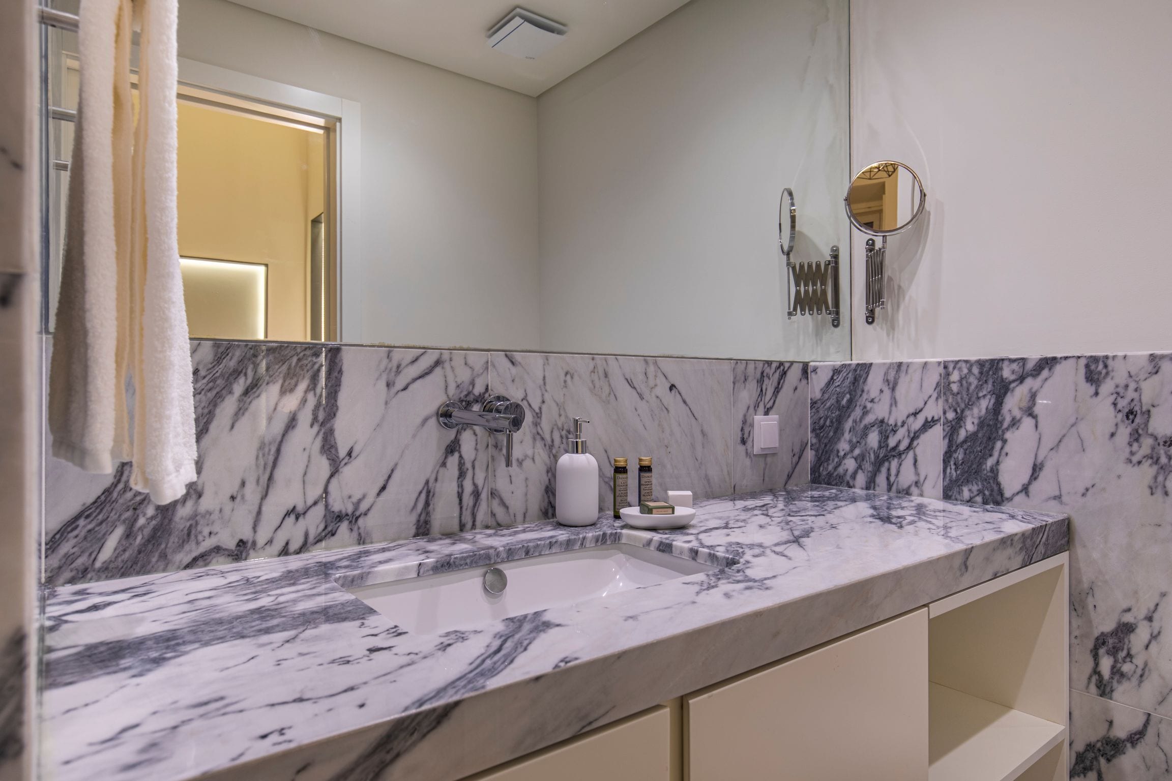 A bathroom with a marble sink, a mirror, and a towel rack.