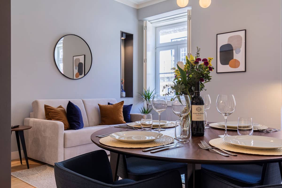Un coin repas avec une table ronde dressée pour quatre personnes, un canapé, un miroir et une œuvre d’art abstraite encadrée accrochée au mur.
