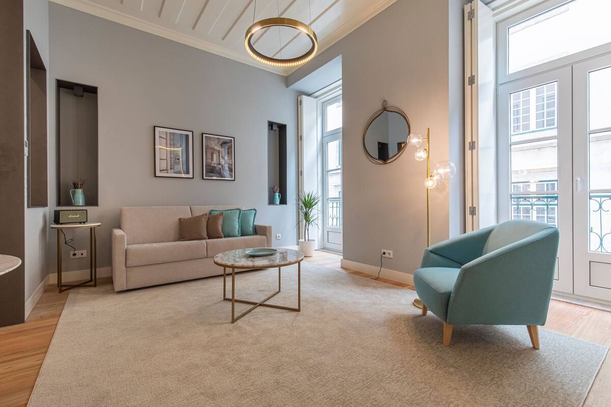 Un salon moderne avec un canapé, une table basse, un fauteuil turquoise et un miroir rond.