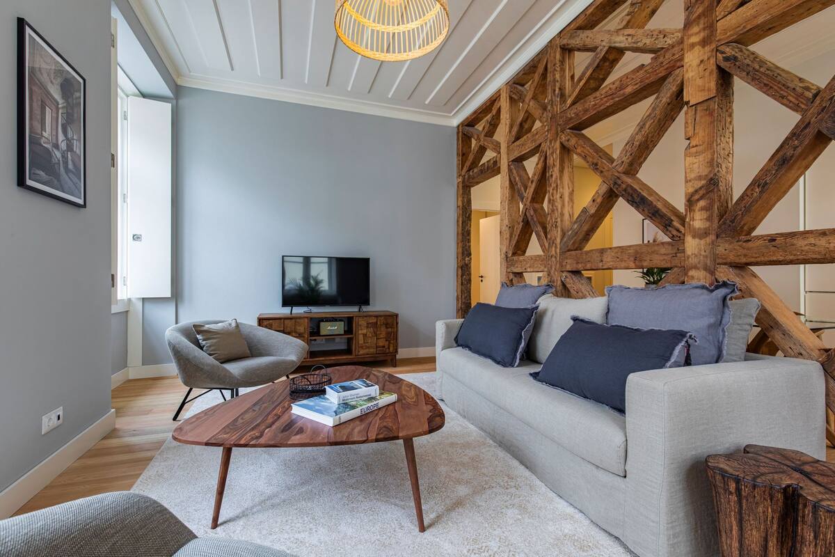 Un salon moderne avec un plafond en bois, un canapé gris, une table basse et un téléviseur.