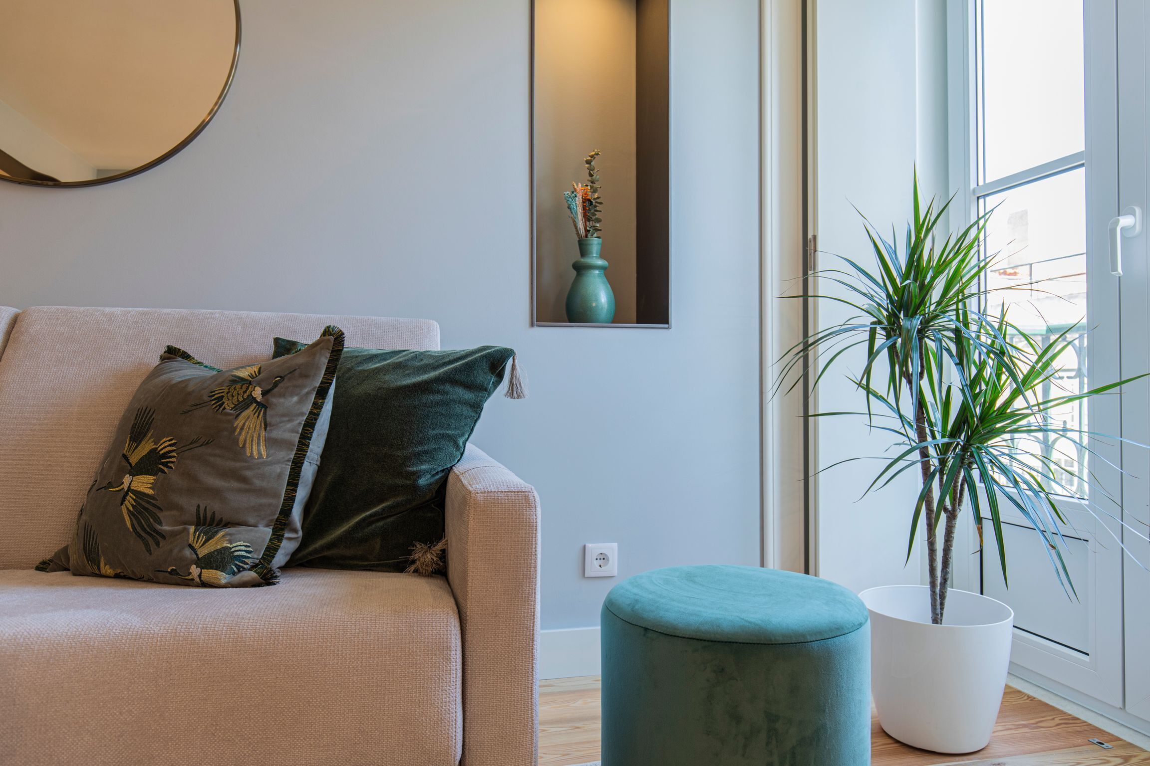 A modern living room with a sofa, a potted plant, and a mirror on the wall.
