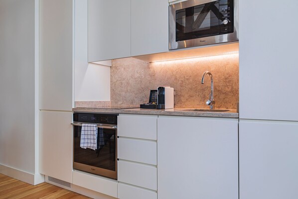 Una cocina moderna con armarios blancos, microondas integrado, cafetera y horno de acero inoxidable.