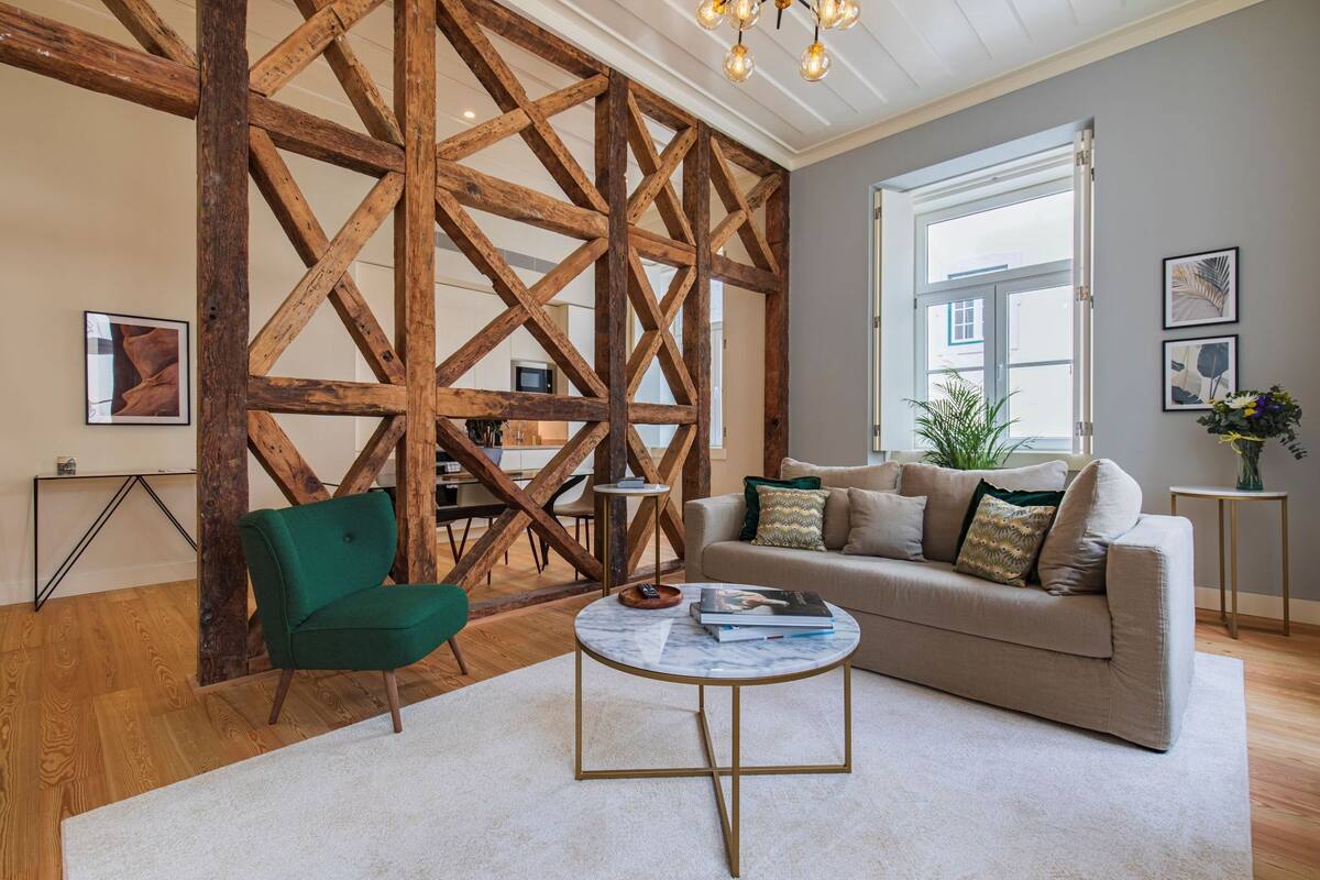 Un salon moderne avec une structure en poutres apparentes, un fauteuil vert, un canapé beige et une table basse en marbre.