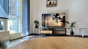 Moderni olohuone, jossa on suuri litteänäyttöinen televisio, puulattia ja ruukkukasveja.