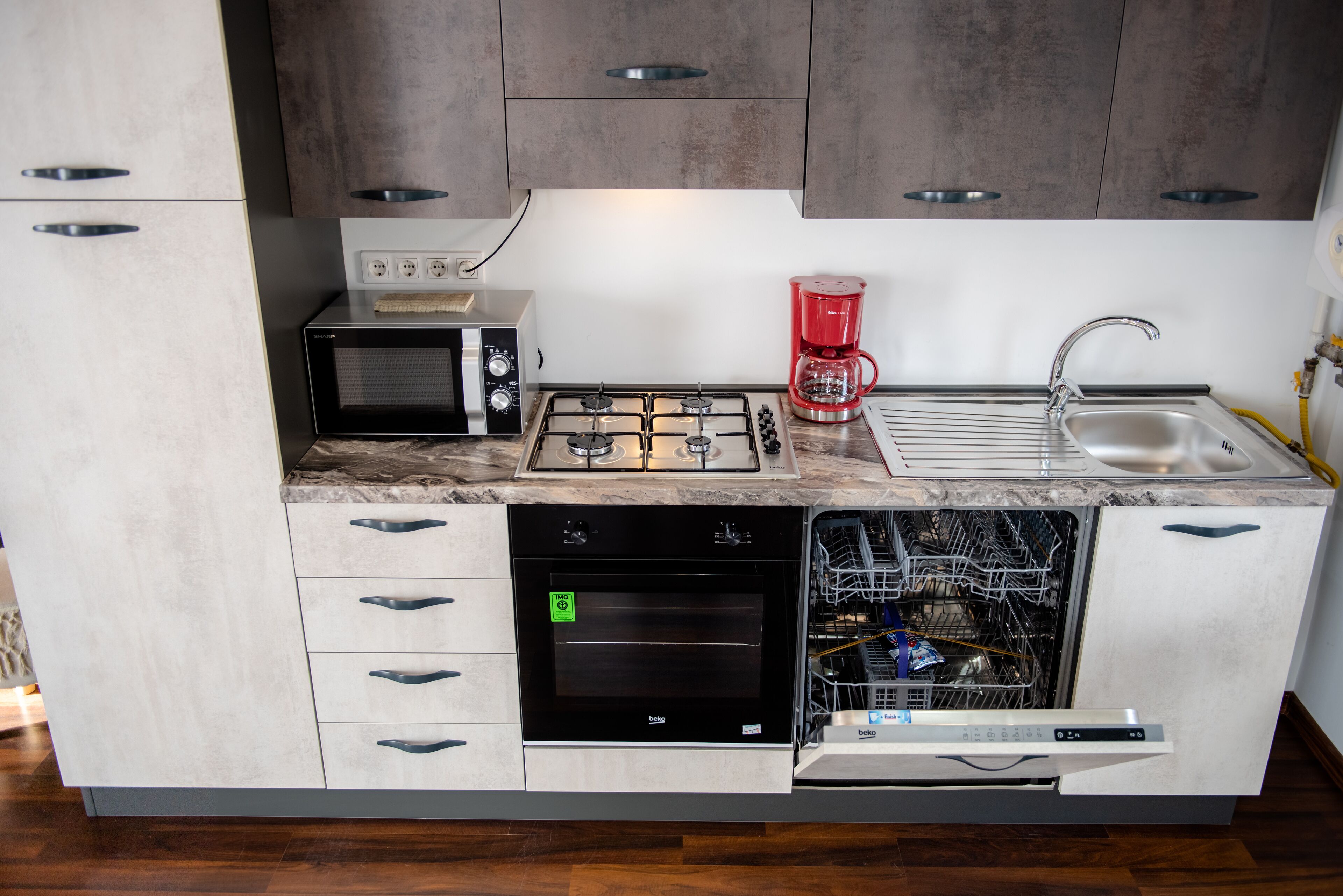 A compact kitchen with a microwave, stove, coffee maker, dishwasher, and a sink.