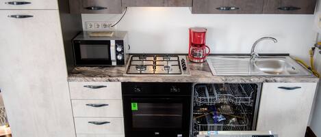 A compact kitchen with a microwave, stove, coffee maker, dishwasher, and a sink.