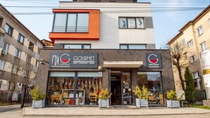 A modern two-story building with a storefront labeled "GOURMET" featuring a variety of food items. - Niagara Apartments (Baia Mare)