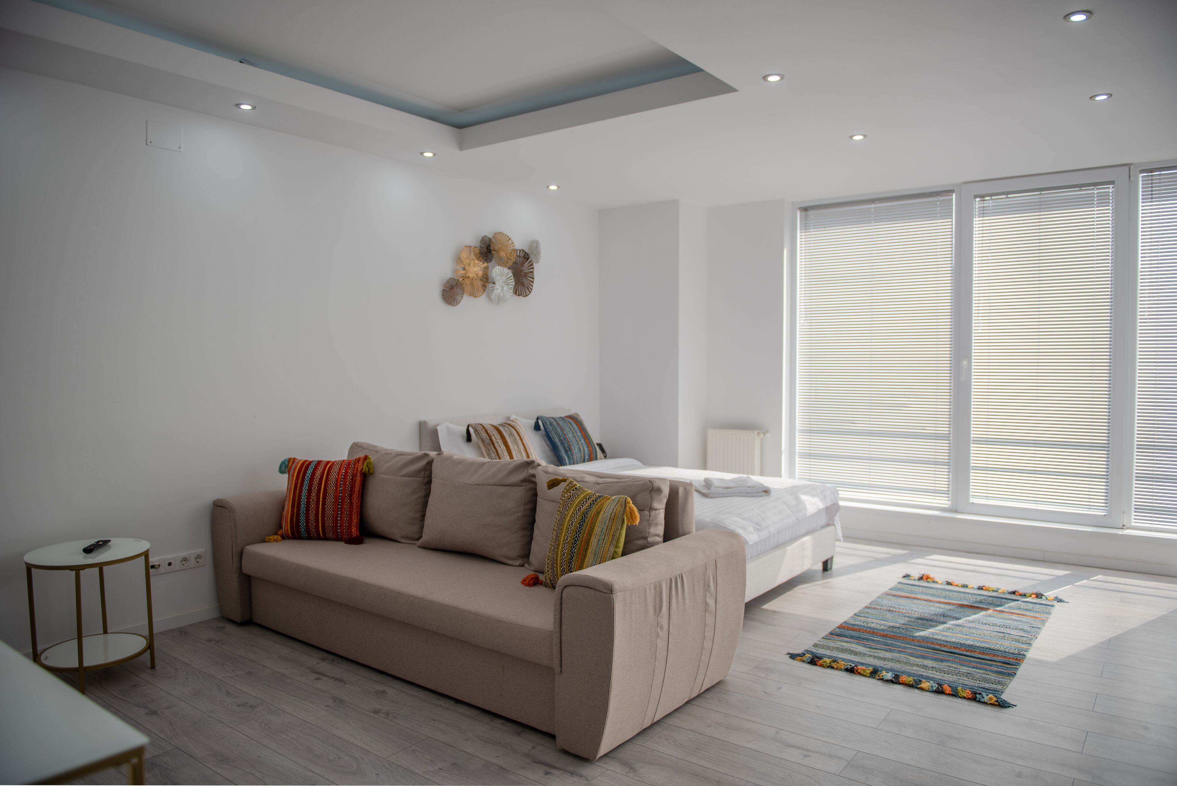 Una camera da letto moderna con un divano beige, un letto con biancheria da letto bianca e un'ampia finestra con tende.