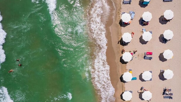 Vista aérea de una playa con hileras de sombrillas y sillas de descanso, lo que sugiere un entorno de resort.
